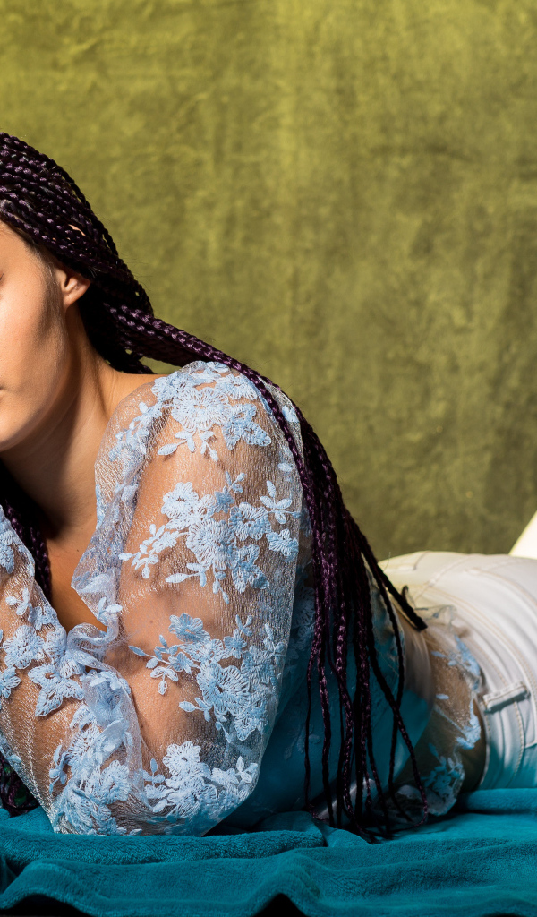 Брюнетка с косами на голове лежит на постели