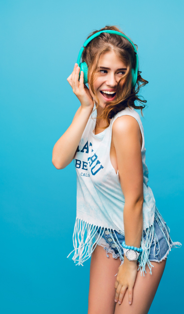 Веселая девушка в наушниках на голубом фоне