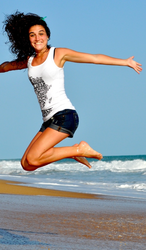 Веселая девушка прыгает на морском берегу