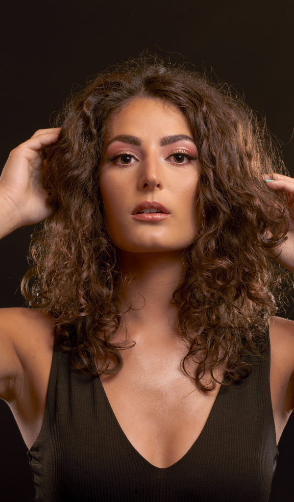 Кудрявая девушка держит руки в волосах на черном фоне