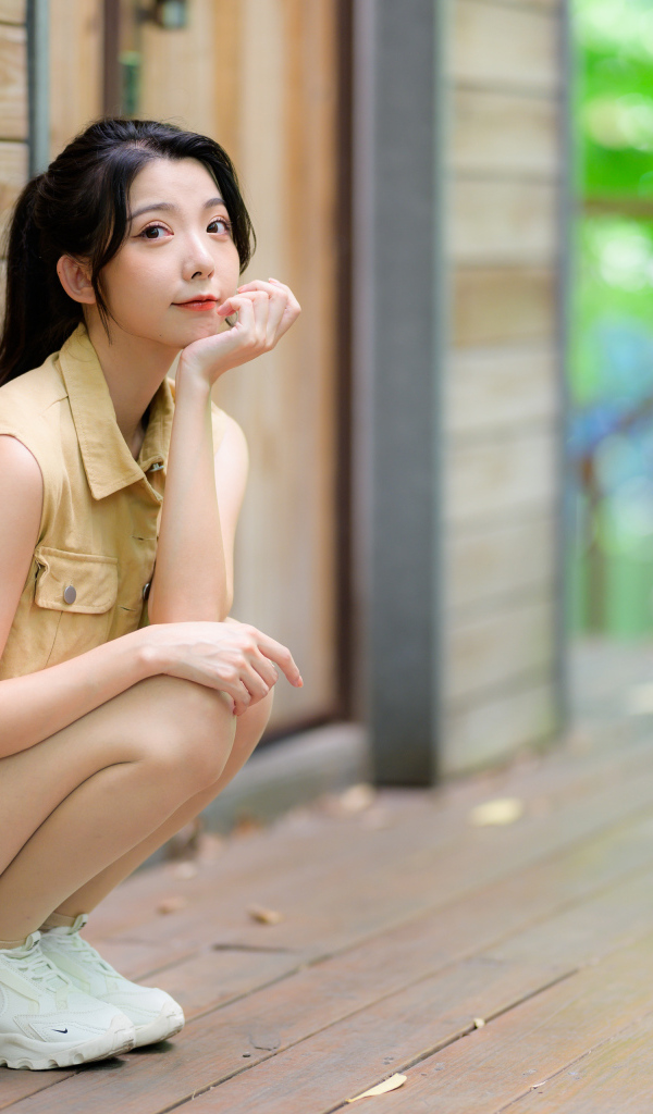 Милая азиатка сидит на корточках у стены