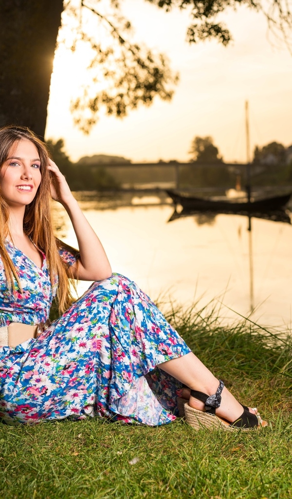 Милая девушка в платье сидит на берегу реки в парке