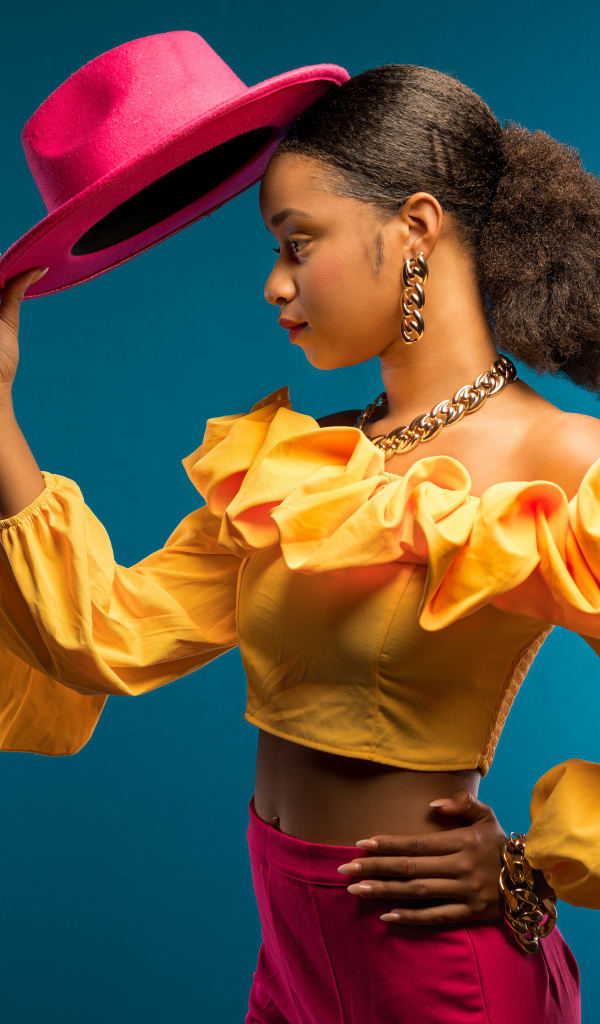 Темнокожая девушка в костюме с красной шляпой в руке