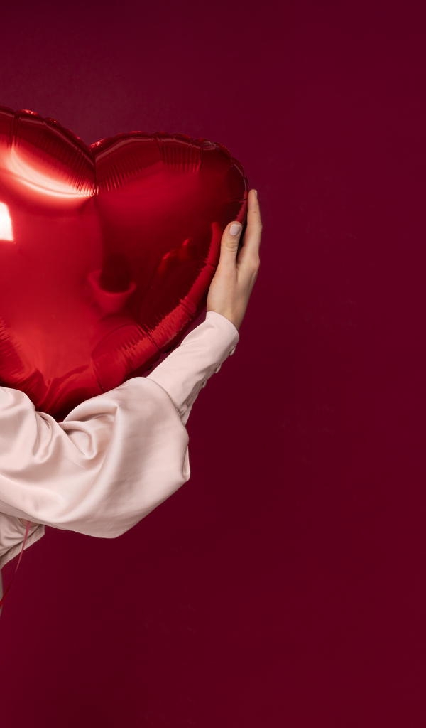 Девушка держит шарик в форме сердца на красном фоне