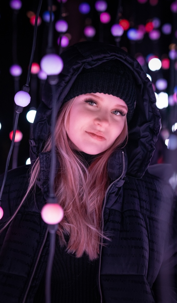 Девушка в черной куртке у светящейся гирлянды