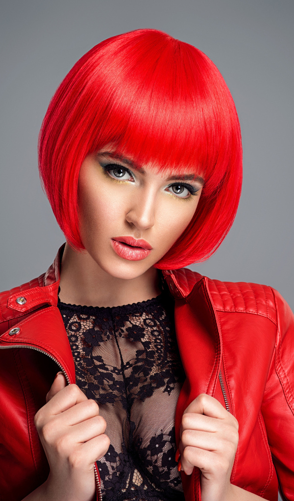 Рыжеволосая девушка с короткой стрижкой в красной кожаной куртке на сером фоне