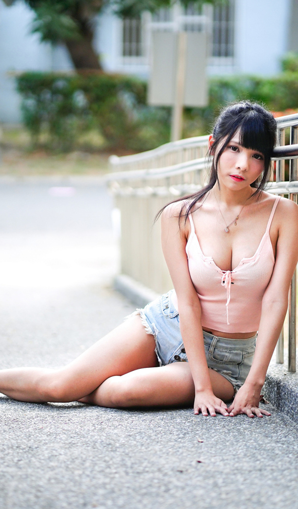 Грустная девушка азиатка сидит на дороге у перил