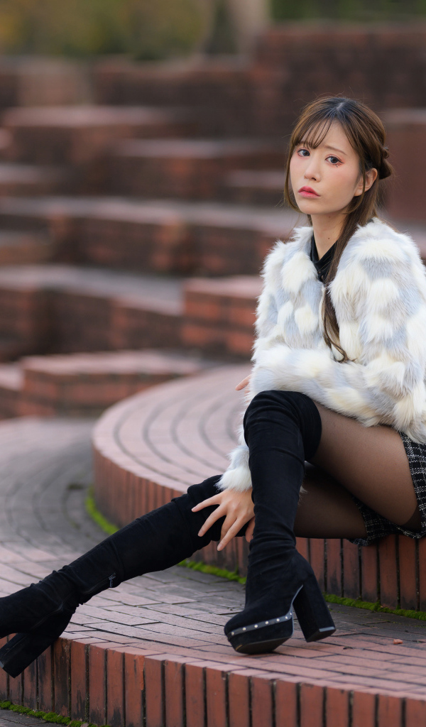 Грустная азиатка в шубе сидит на ступеньках