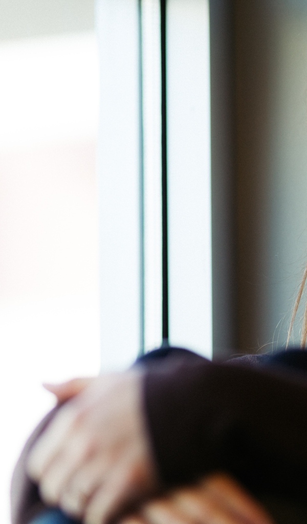 Грустная девушка сидит у окна