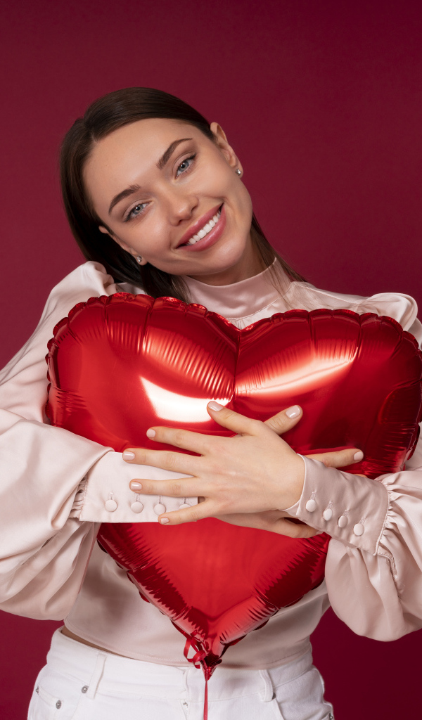 Улыбающаяся девушка обнимает шар в форме сердца
