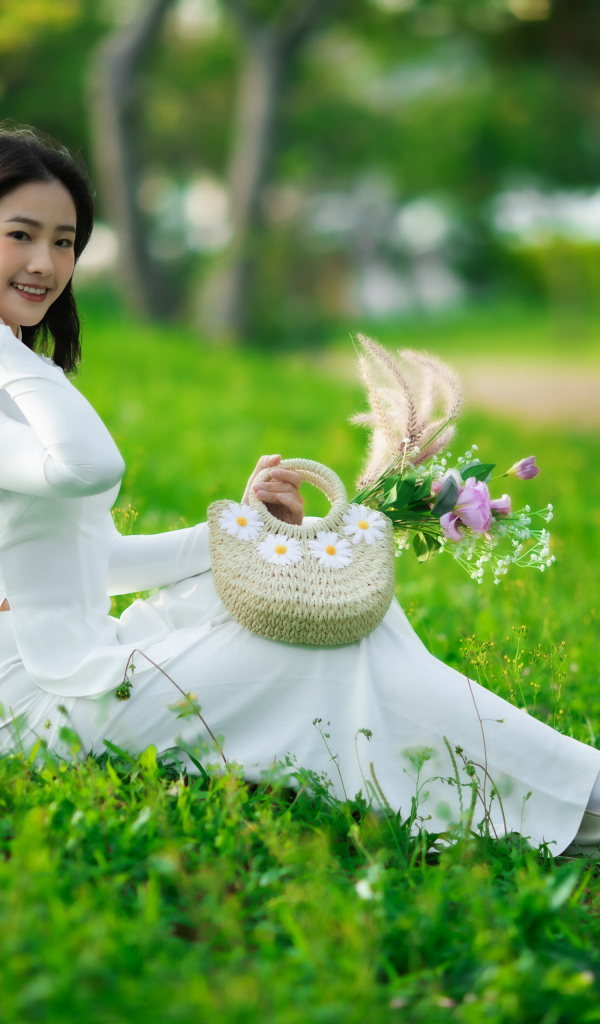 Нежная азиатка в белом наряде сидит на траве