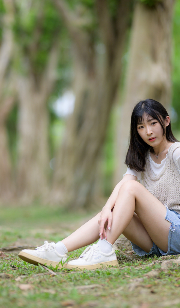 Молодая девушка азиатка сидит у дерева в парке