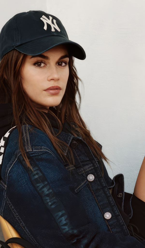 Красивая модель Кайя Гербер в кепке сидит у стены
