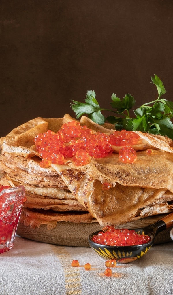 Блины на столе с икрой, маслинами и бутылкой спиртного на Масленицу