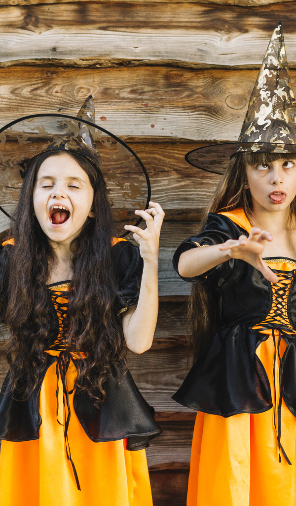 Две девочки в костюме ведьмы у стены на Хэллоуин
