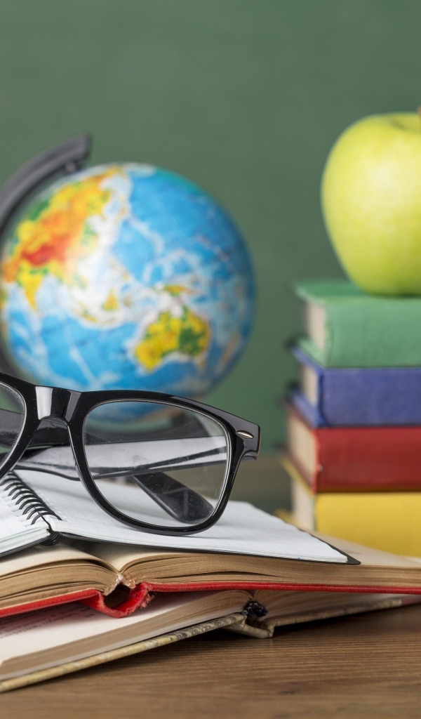 Книги, очки и карандаши с глобусом на столе у доски