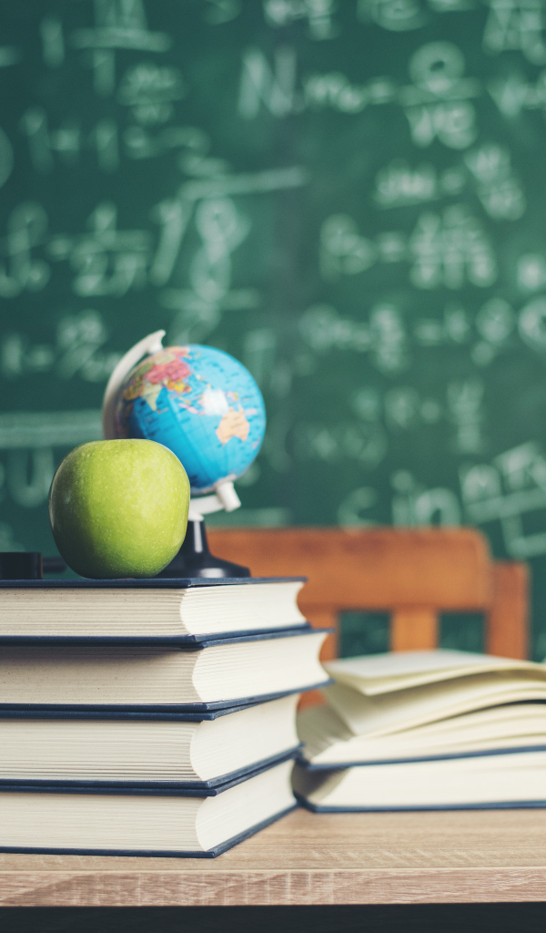 Книги на столе с зелеными яблоками и глобусом на фоне доски