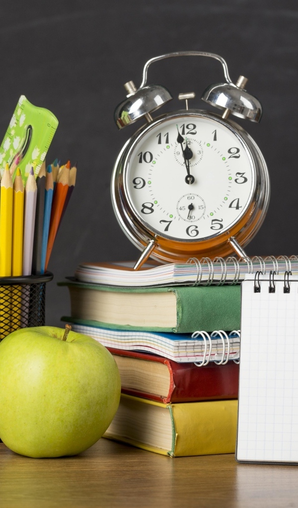 Канцелярские предметы на столе с будильником и книгами 