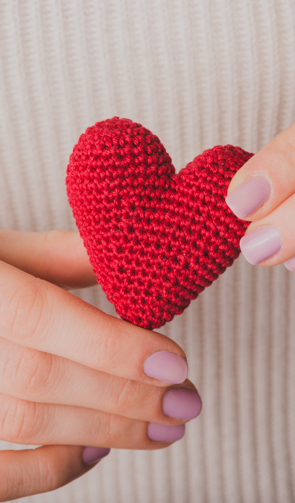 Девушка держит в руке вязаное красное сердце
