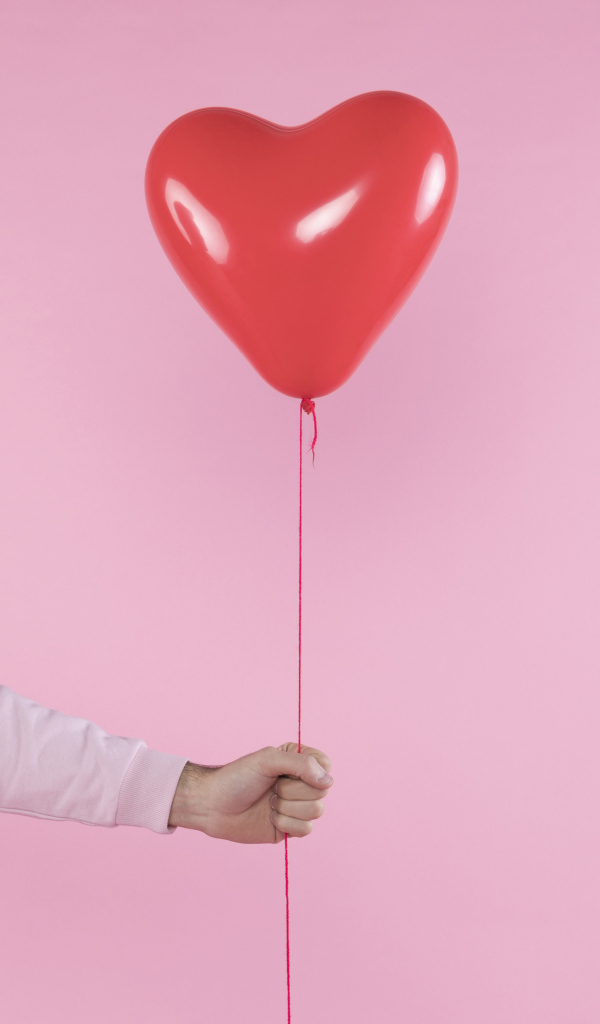 Шарик в форме сердца в руке на розовом фоне