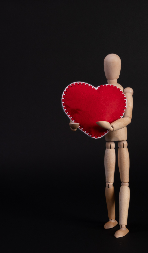 Марионетка держит красное сердце на черном фоне