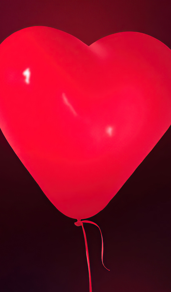 Красный шарик в форме сердца на фоне стены
