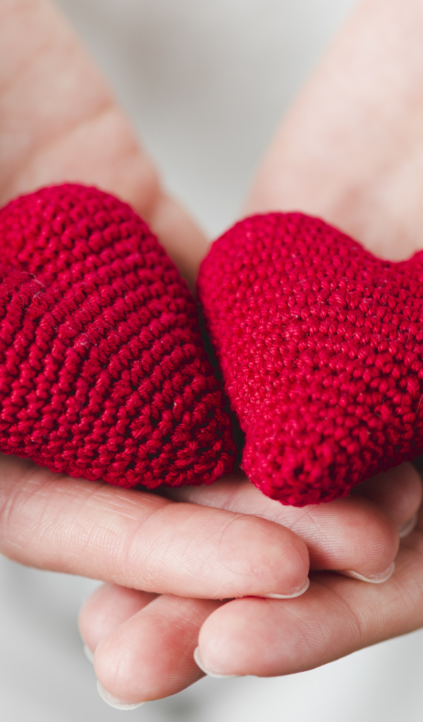 Два красных вязаных сердечка в руках девушки