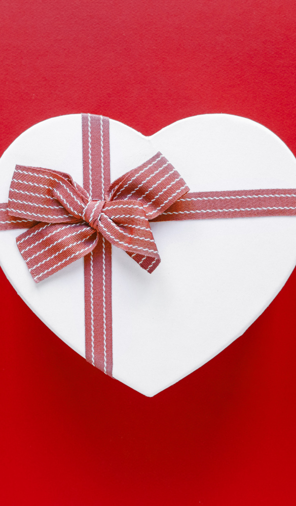 Белая коробка в форме сердца с бантом на красном фоне