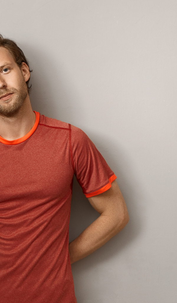 Мужчина в футболке стоит у серой стены