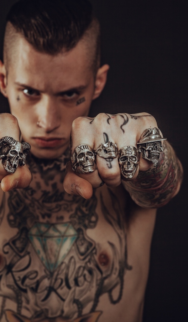 Мужчина с татуировками на теле показывает перстни на пальцах