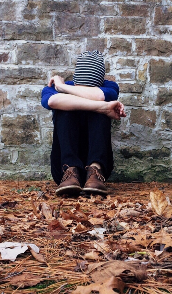 Молодой парень сидит у стены с закрытым лицом