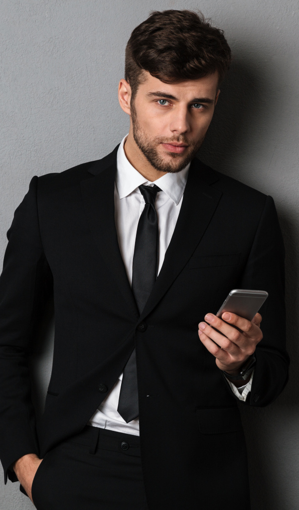 Деловой мужчина в костюме стоит у стены с телефоном