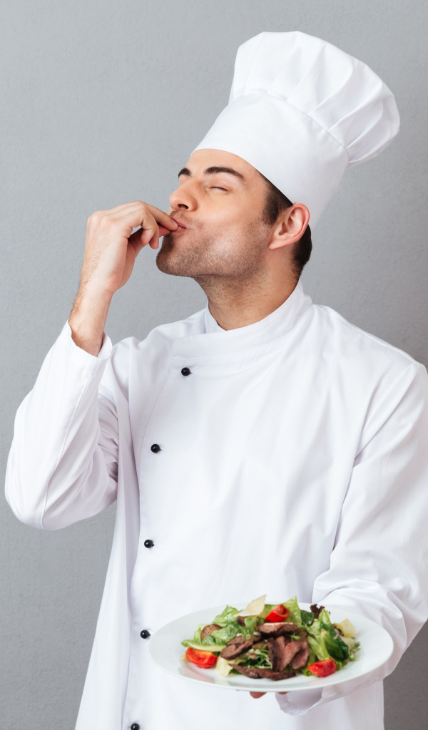 Мужчина повар в белом костюме с блюдом на сером фоне