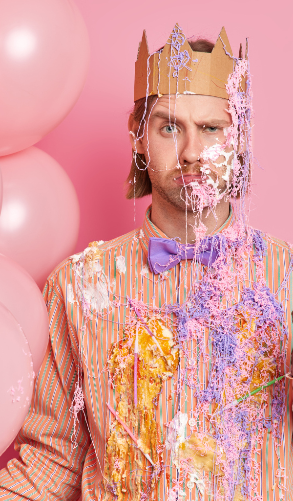 Мужчина принц с тортом и шариками на розовом фоне