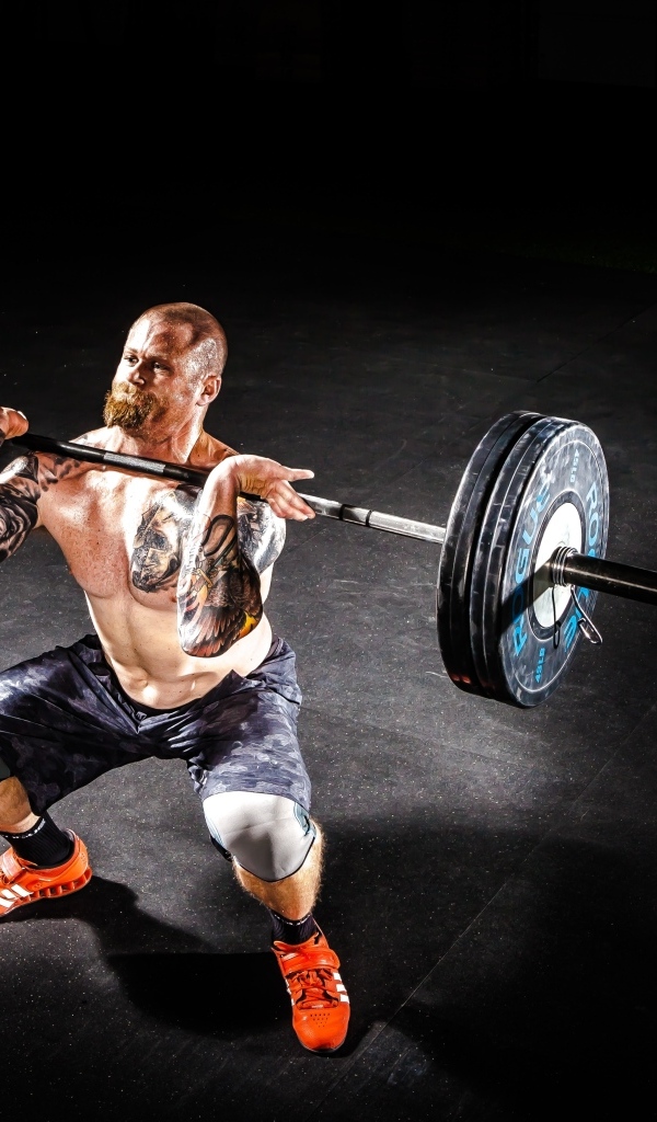 Сильный мужчина с татуировками на теле поднимает штангу