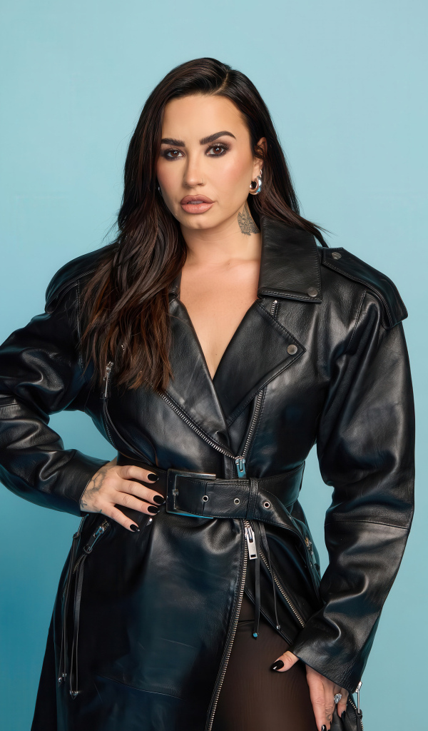 Певица Деми Ловато в кожаном черном пальто на голубом фоне