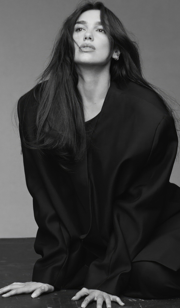 Певица Дуа Липа в черном костюме сидит на полу