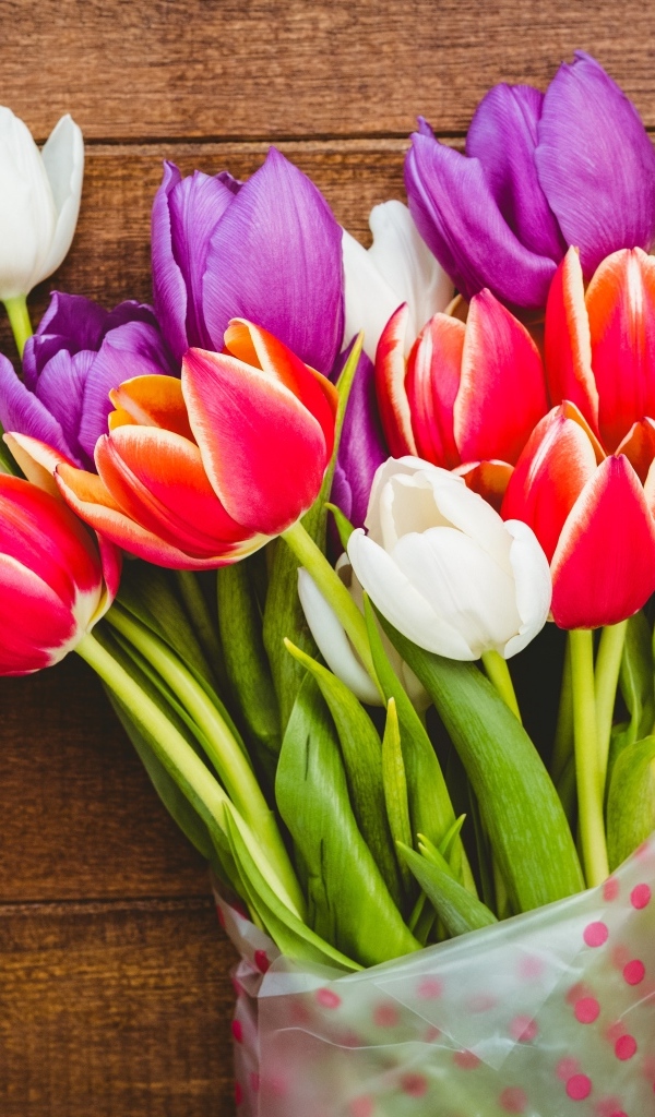 Букет разноцветных тюльпанов в пакете на деревянном фоне