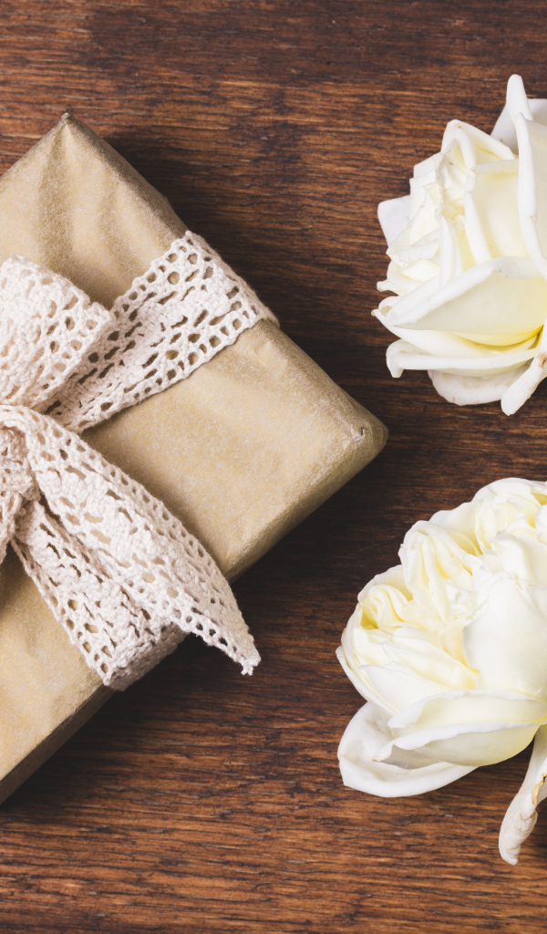 Коробка с подарком на деревянном столе с белыми розами