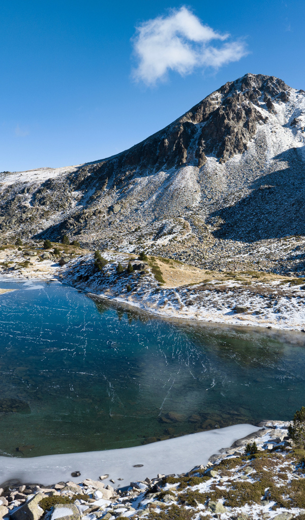 Покрытое льдом озеро в заснеженных горах в лучах солнца, Андорра