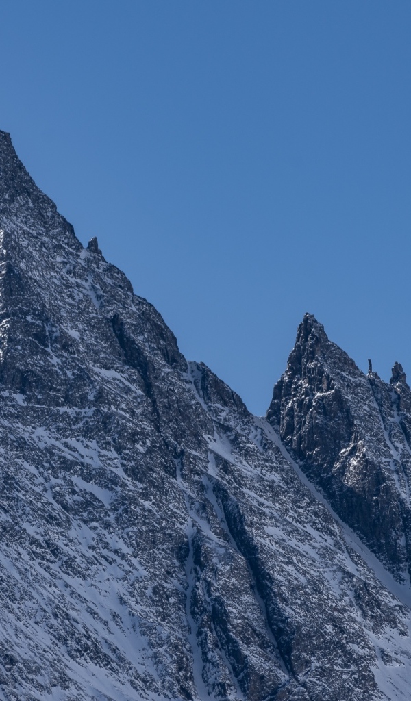 Крутая вершина горы в снегу на фоне голубого неба