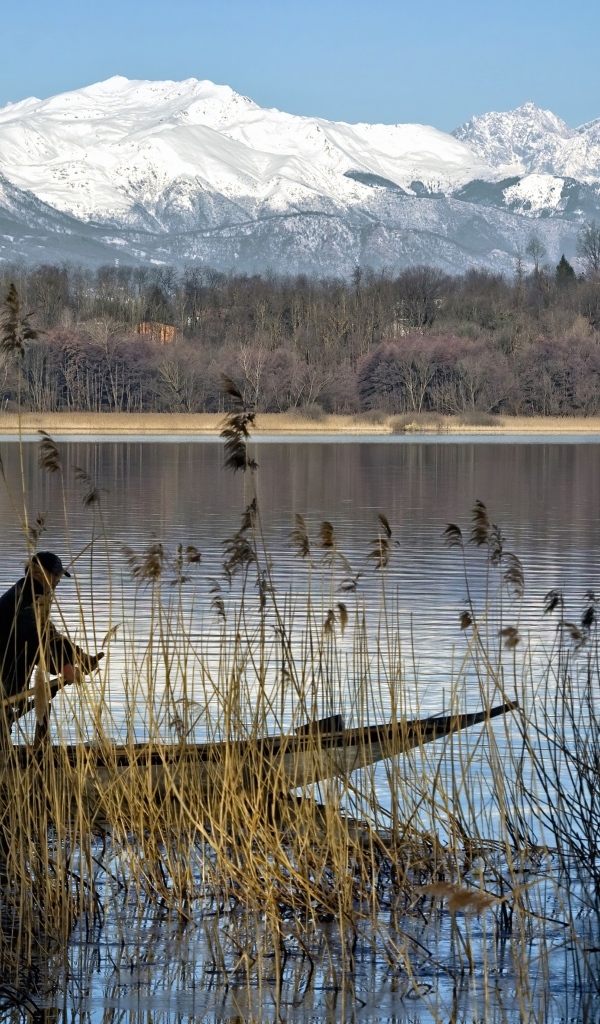 Рыбак плывет по воде на фоне заснеженных гор