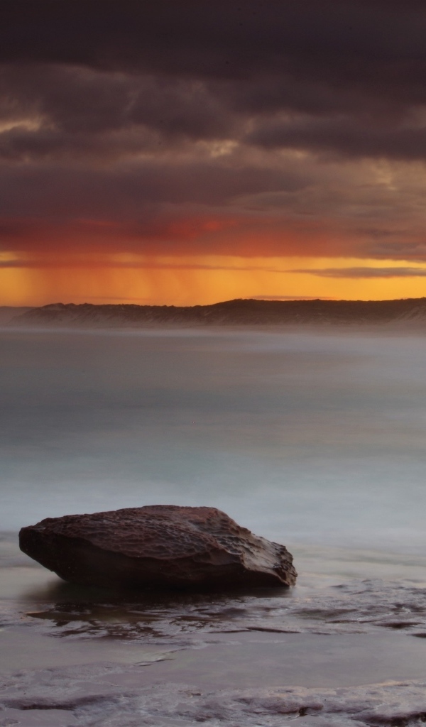 Большой камень в воде на фоне грозового неба в море