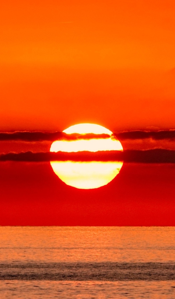 Яркое солнце в облаках на закате над морем 