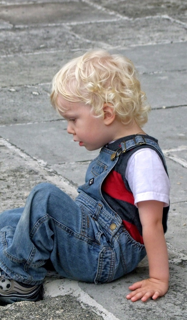 Мальчик в джинсовом комбинезоне сидит на дороге