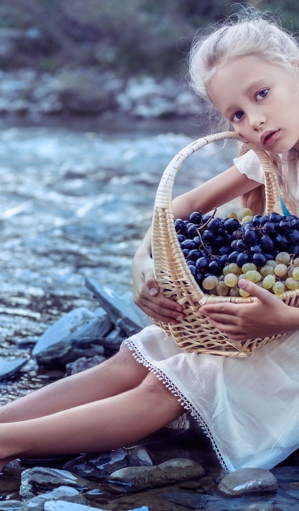 Девочка с корзиной винограда сидит у воды
