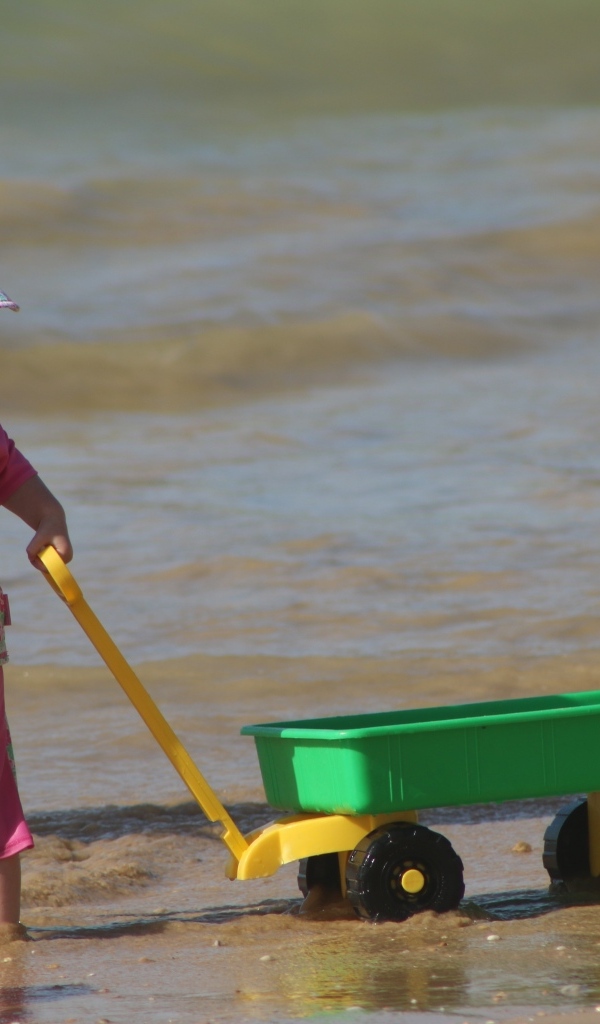 Девочка с машинкой играет на песке у моря