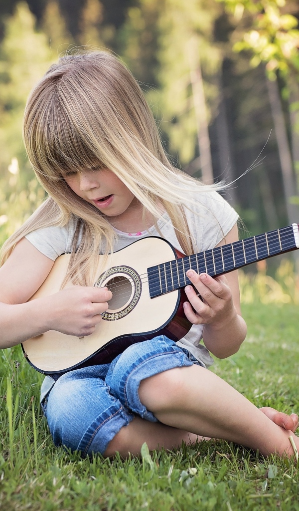 Девочка с маленькой гитарой сидит на траве