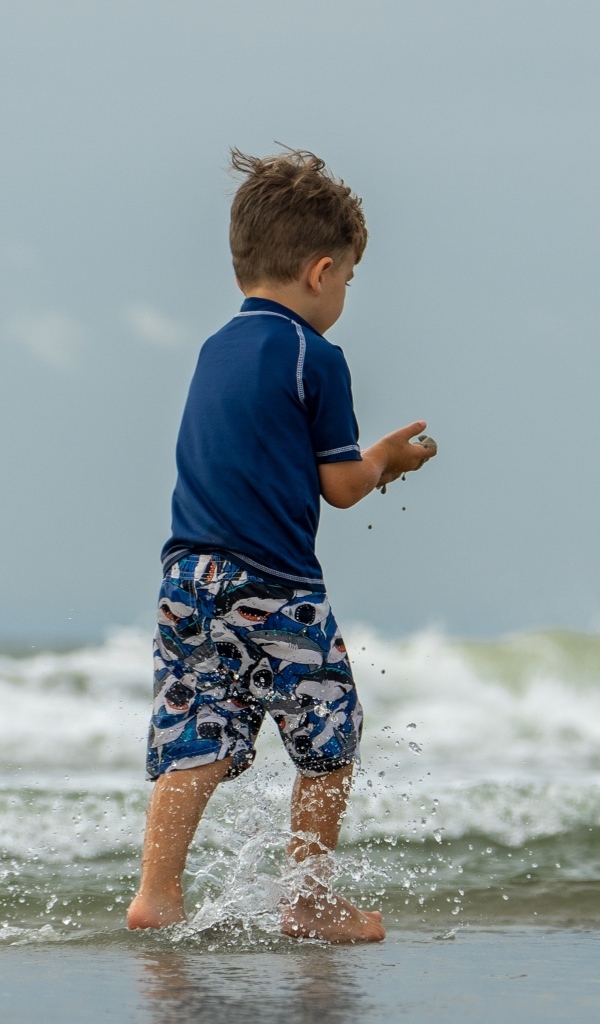 Маленький мальчик гуляет по воде у моря