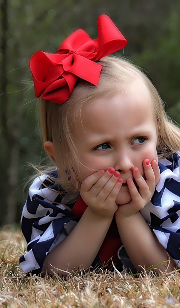 Маленькая девочка с красным бантом на голове лежит на траве
